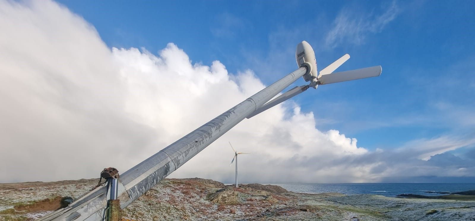 A small wind turbine lowered on its tower for servicing on a coastal site